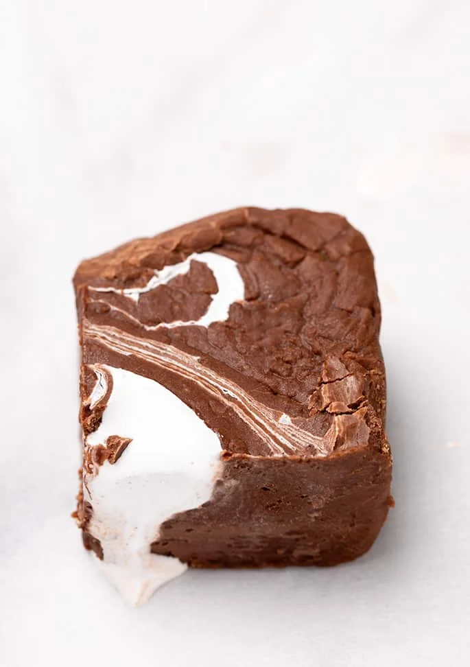 One piece of fudge with marshmallow fluff on top, dripping down the side on white paper