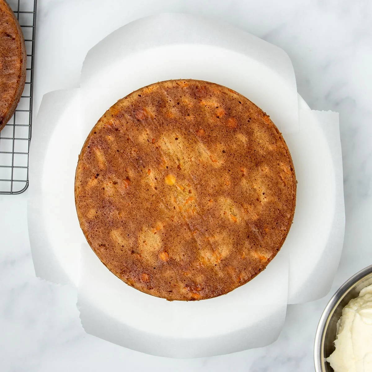 One round light brown carrot cake overturned on four strips of white parchment paper.