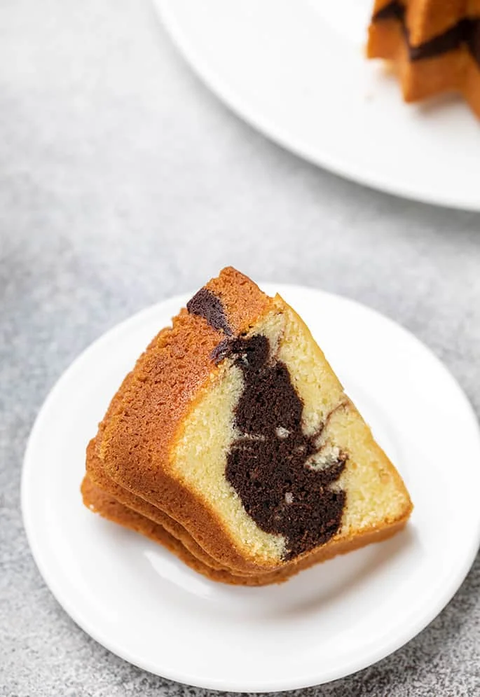 One slice of marble bundt cake on small white dessert plate on marbled gray and white surface