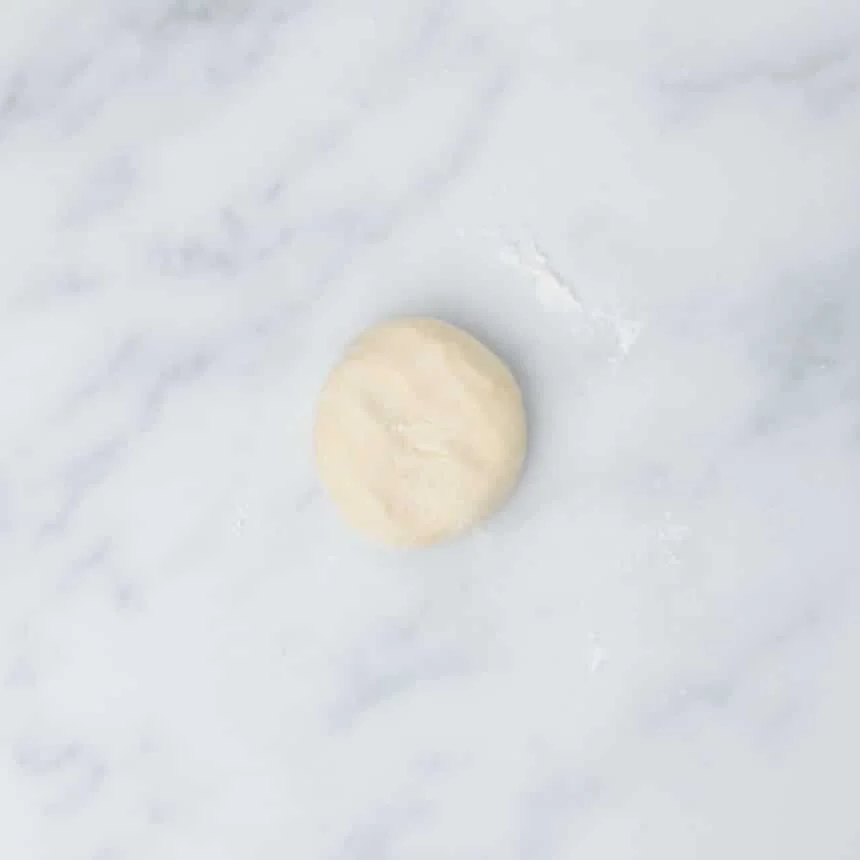 one smooth small piece of dough in a round disk on a marble surface with white flour