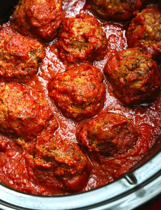 Overhead image of 12 to 14 tomato sauce covered meatballs in black crock pot liner