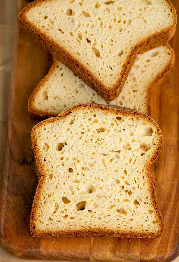 Overhead image of 3 overlapping slices of potato bread on brown cutting board.