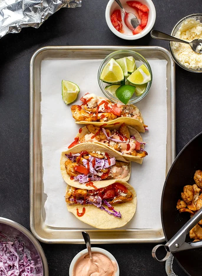 Overhead image of 4 corn tortillas with taco fillings on white paper-lined metal tray