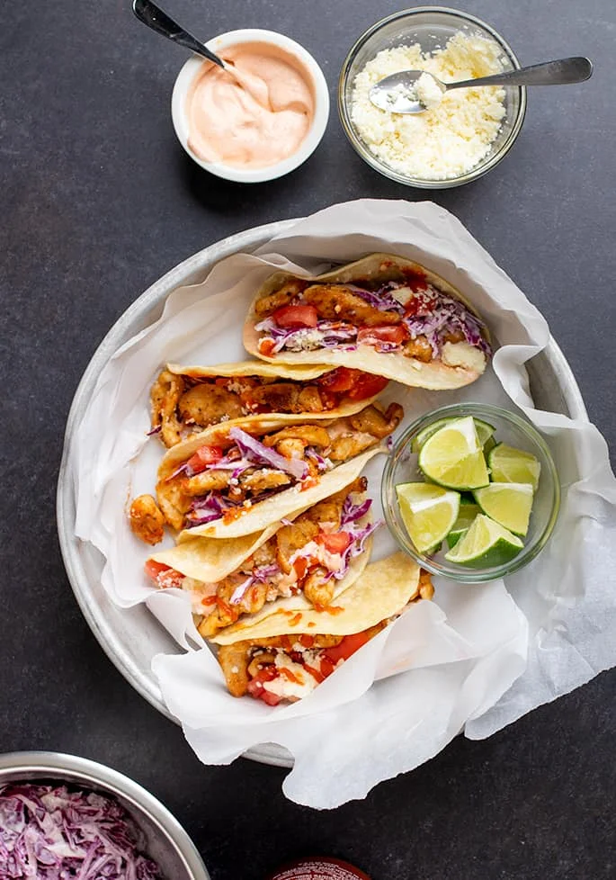 Overhead image of 5 corn tortillas with taco fillings in white paper in a round metal tin