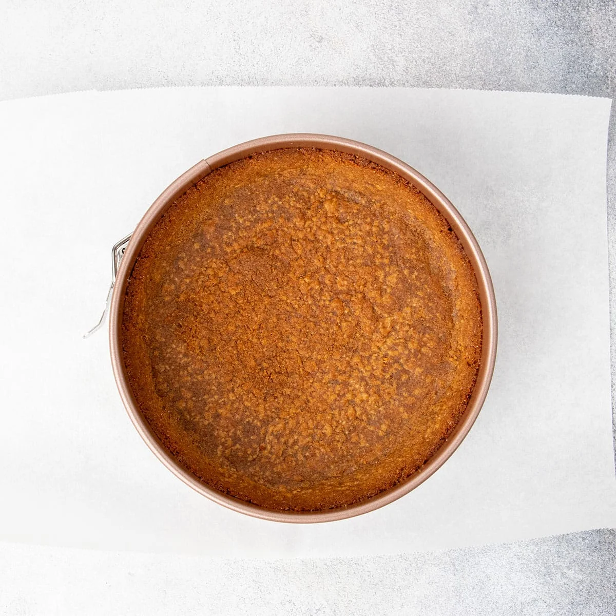Overhead image of baked graham cracker crust in springform pan on white paper.