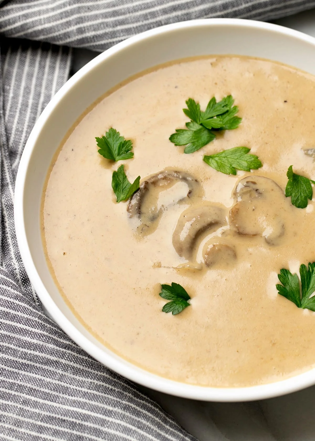 Overhead image of cream of mushroom soup with sliced cooked mushrooms and parsley on top with gray and white striped cloth