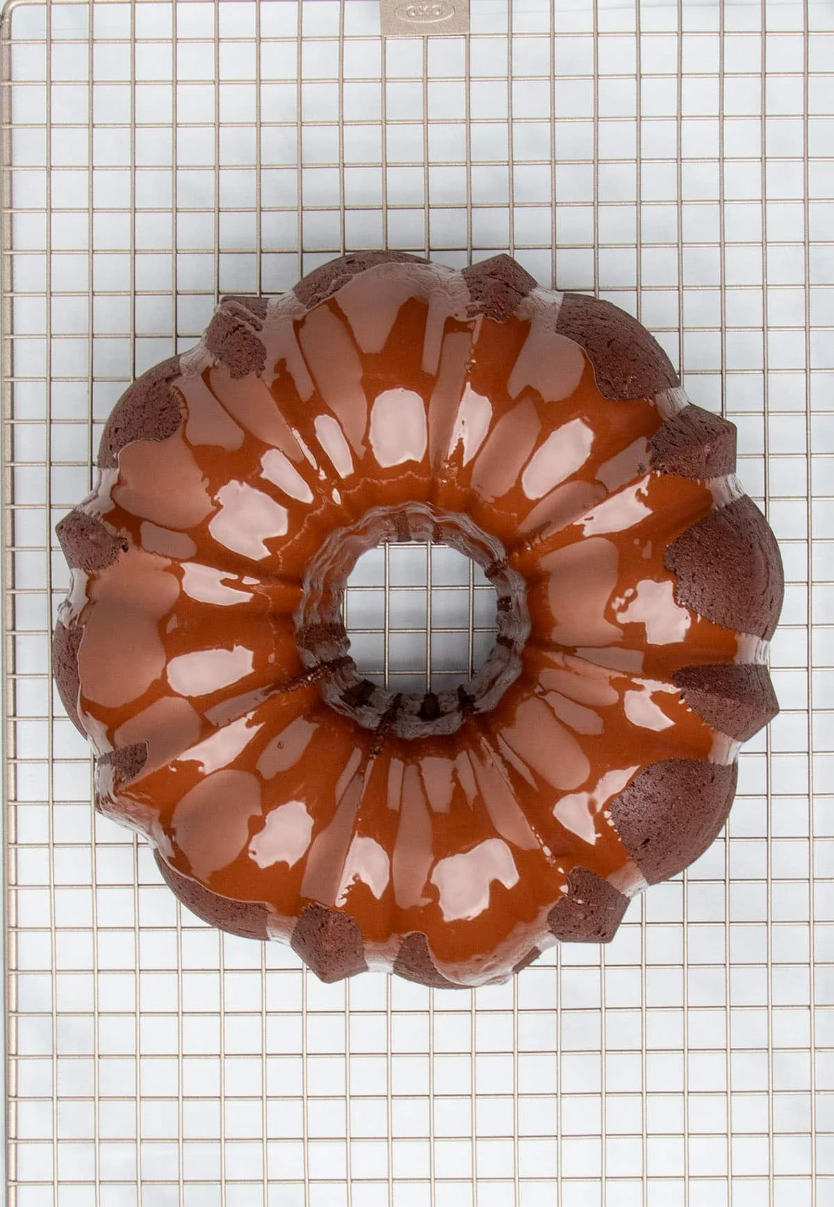 overhead image of fresh shiny brown chocolate glaze on dark brown chocolate bundt cake on gold colored wire rack