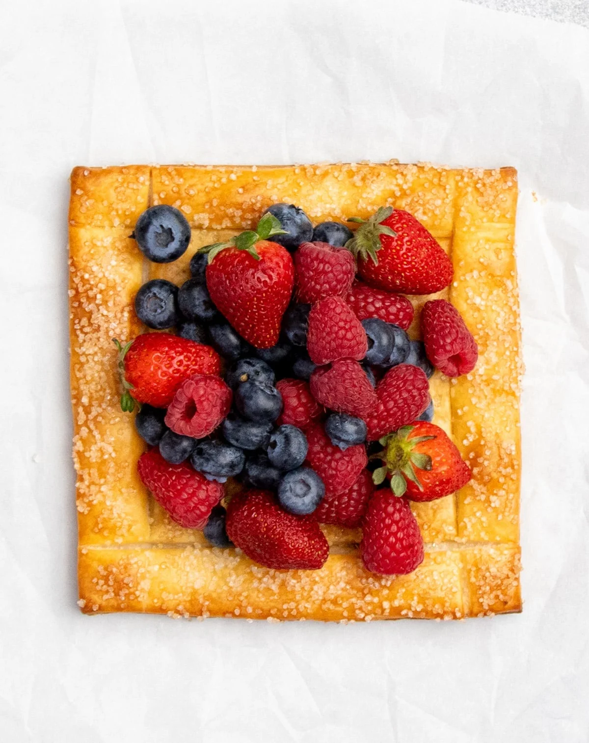 Overhead image of golden brown pastry square with strawberries, blueberries and raspberries in center.