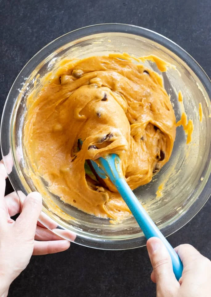 Overhead image of hands holding a bowl of gluten free pumpkin chocolate chip square batter, stirring