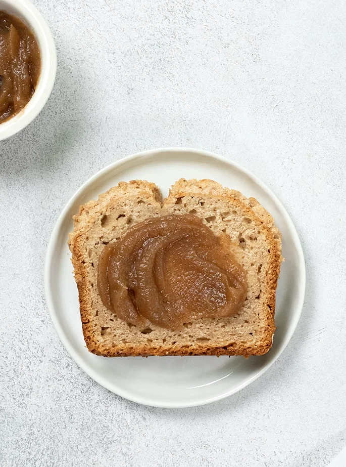 Overhead image of one slice of apple butter bread on a small white plate with apple butter on top