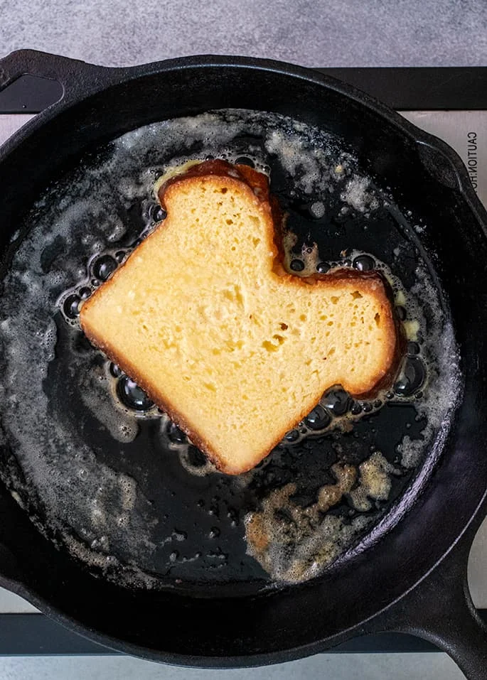 Overhead image of one slice of bread frying in a cast iron skillet with butter