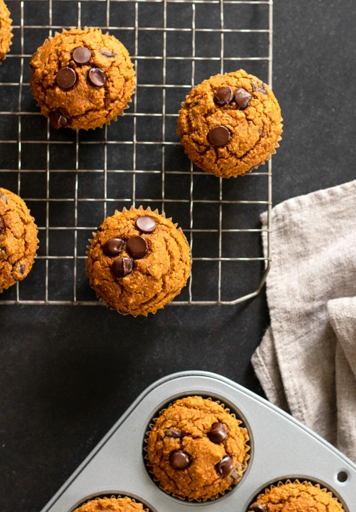 Overhead image of pumpkin muffins with chocolate chips in muffin tin and cooling on wire rack