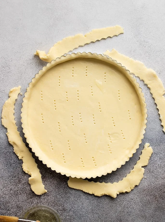 Overhead image of raw tart crust in pan with scraps on sides of pan.