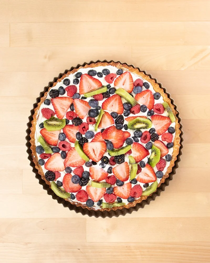Overhead image of round tart pan with fruit tart with sliced strawberries, blackberries, blueberries, sliced kiwi.