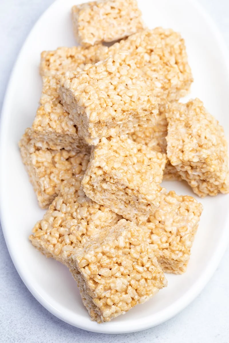 Overhead image of squares of gluten free rice krispie treats in pile on white oval serving dish