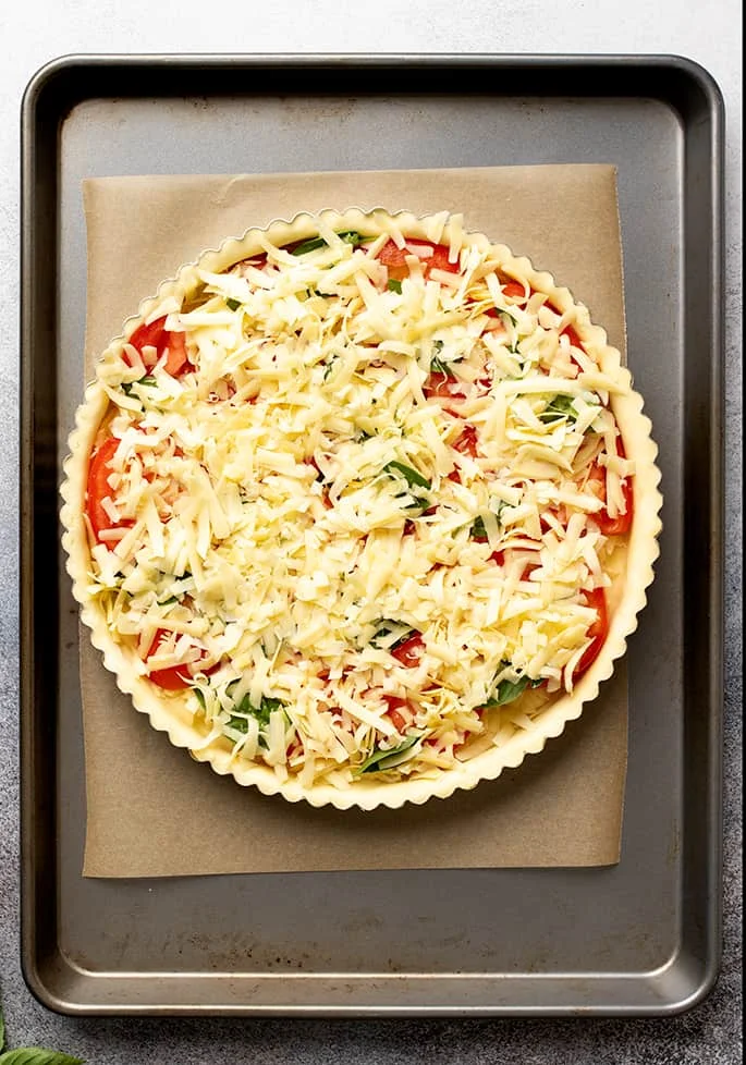 Overhead image of unbaked tomato tart on brown paper on metal baking sheet.