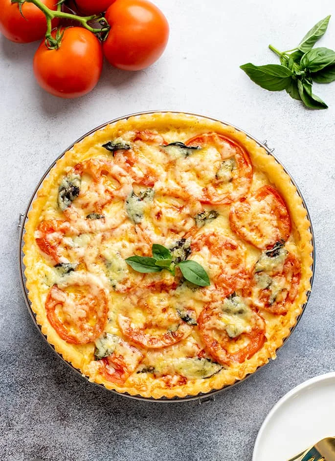 Overhead image of whole baked tomato tart with whole tomatoes and basil leaves.