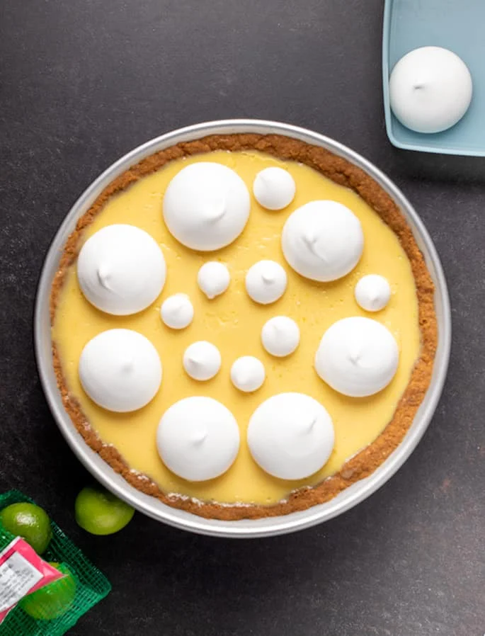 Overhead image of whole key lime pie with meringues and key limes on table