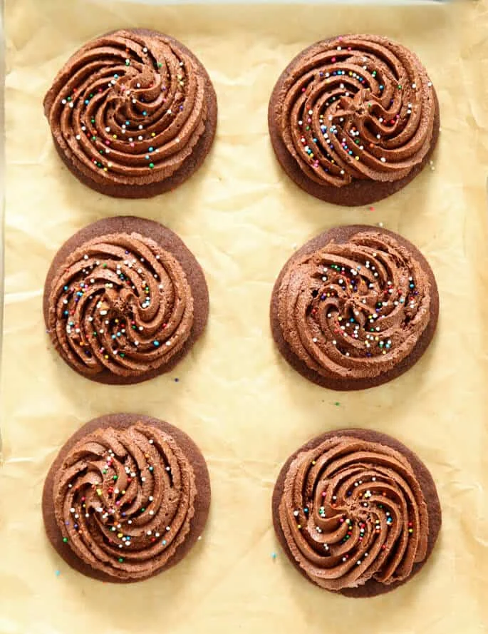 Overhead view of 6 chocolate cutout cookies with nonpariels on beige paper 