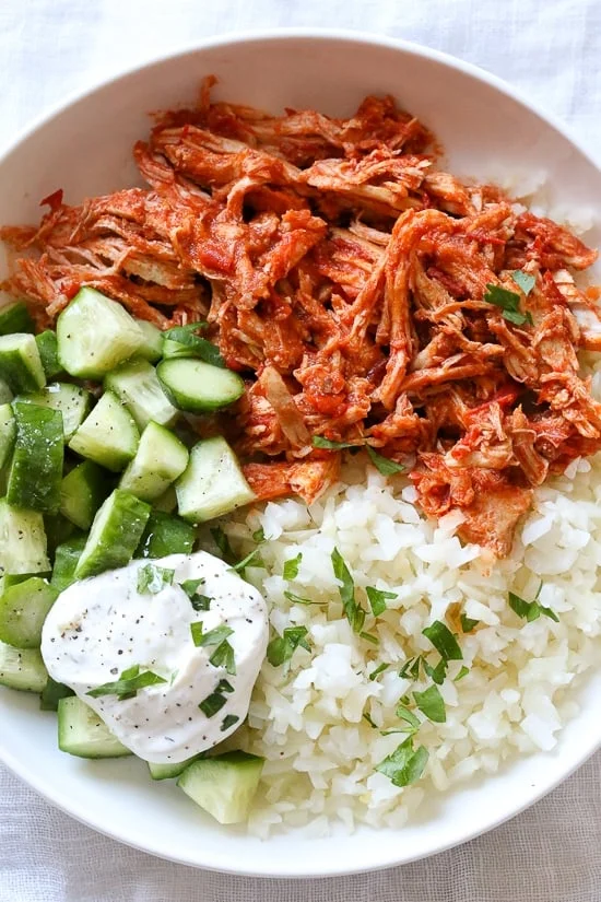 Overhead view of a harissa chicken bowl with yogurt sauce, cucumber, and rice.