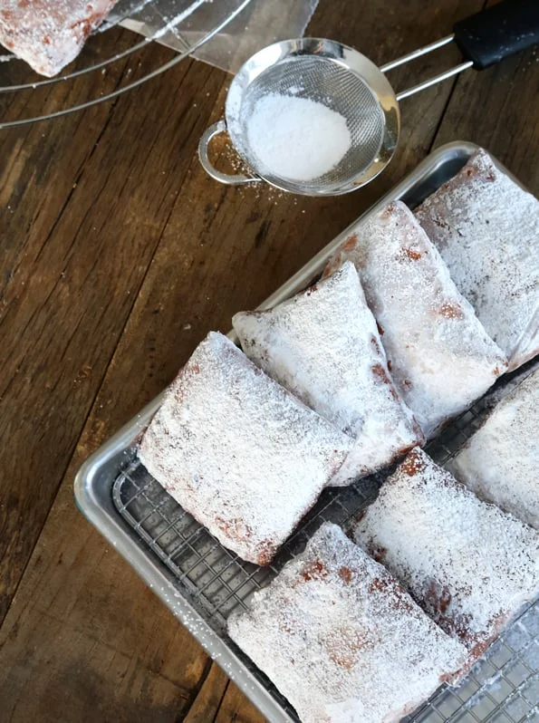 Overhead view of Beignets coated with powdered sugar on metal tray