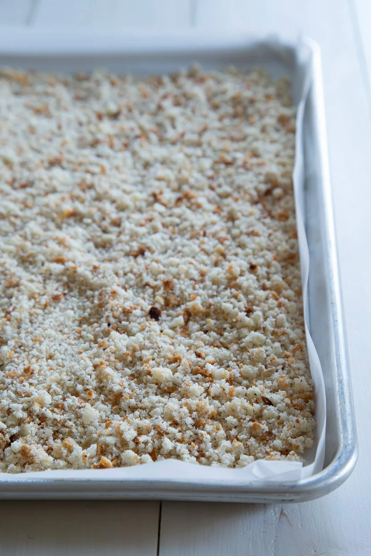 Overhead view of bread crumbs on metal tin lined with white parchment paper.
