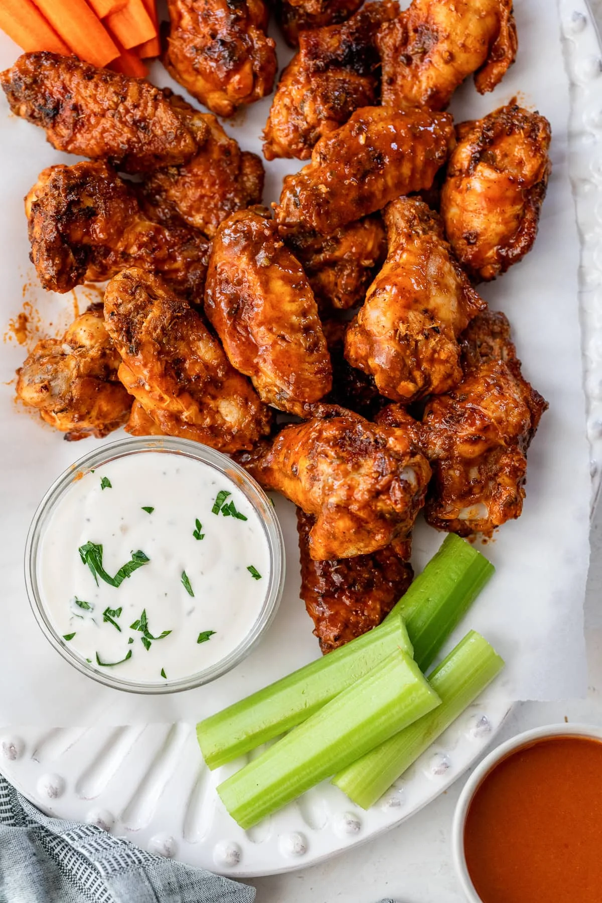 Overhead view of buffalo wings on a platter next to a bowl of blue cheese dressing and celery sticks.