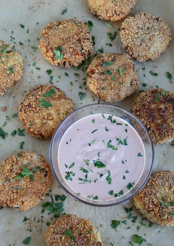 Overhead view of cauliflower fritters and sauce on white surface