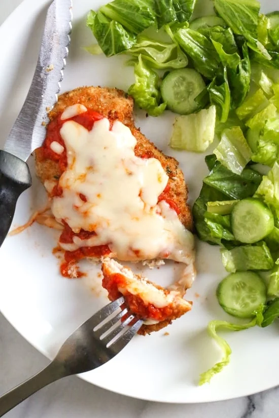 Overhead view of chicken parmesan next to salad on a plate.