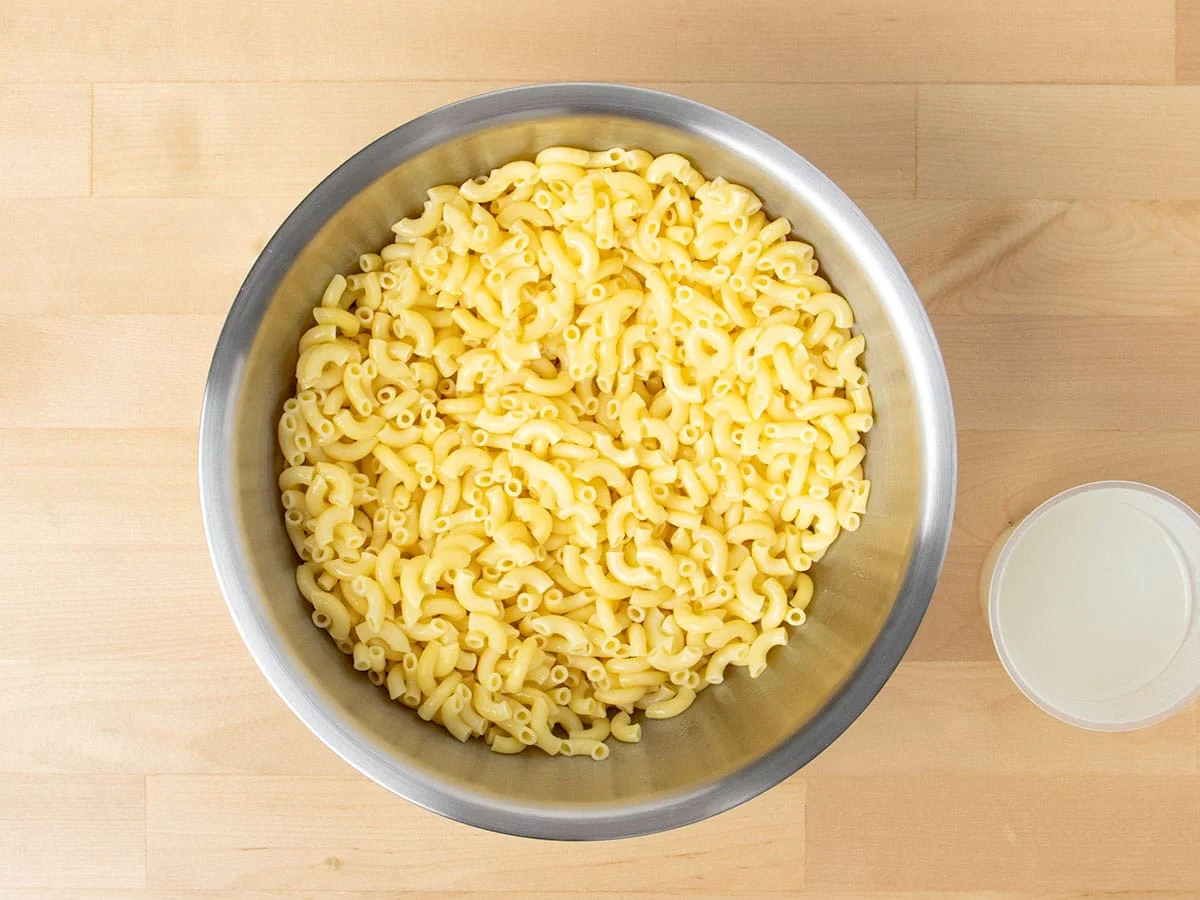 Overhead view of cooked elbow noodles with cup of pasta water.