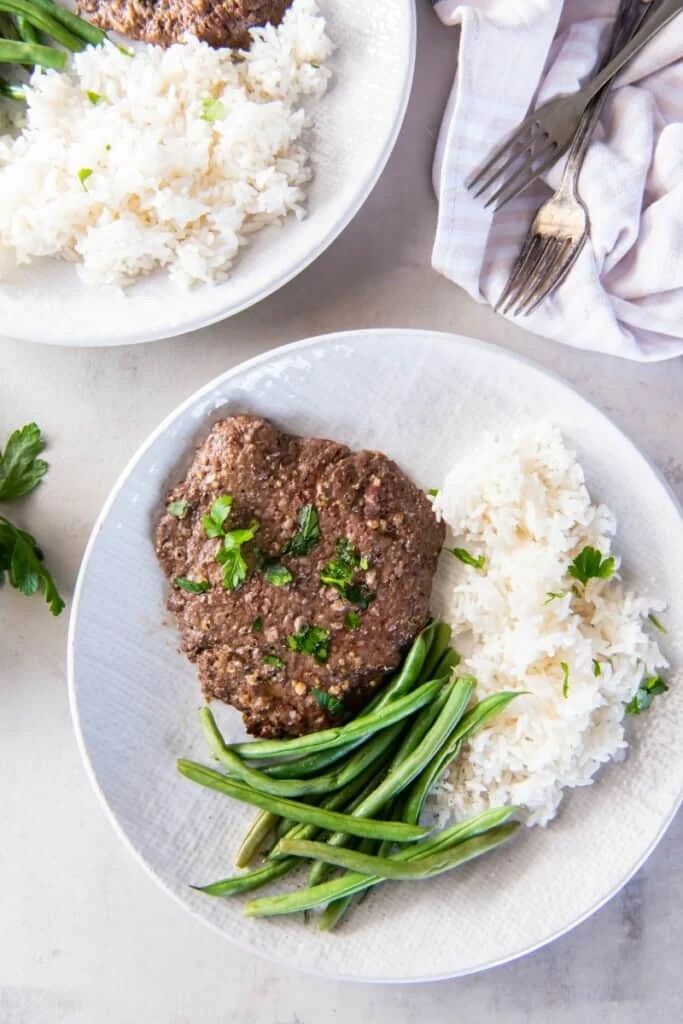 Overhead view of cube steak with rice and green  beans.
