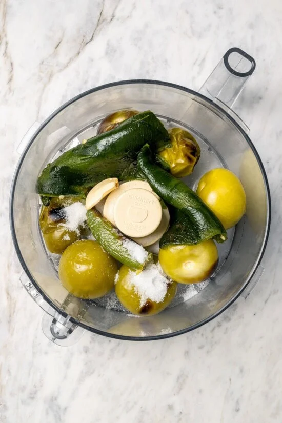 Overhead view of garlic, salt, peppers, and poblanos in food processor bowl