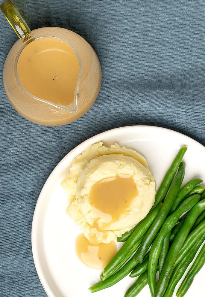 Overhead view of gravy in a glass boat with mashed potatoes, gravy and string beans. 