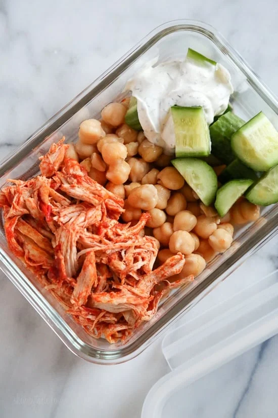 Overhead view of harissa chicken with yogurt sauce, cucumber, and rice in a meal prep container.