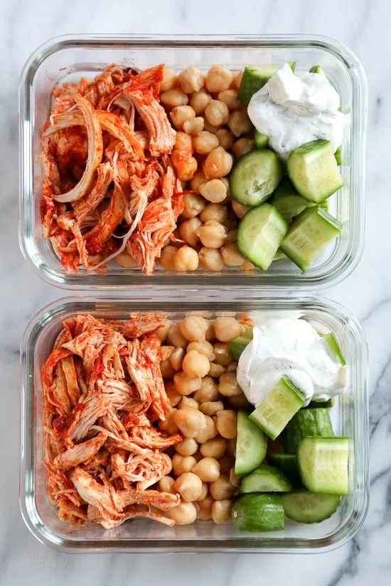 Overhead view of harissa chicken with yogurt sauce, cucumber, and rice in two meal prep containers.