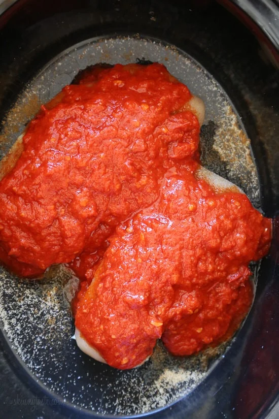 Overhead view of harissa sauce added to chicken breasts inside the slow cooker.