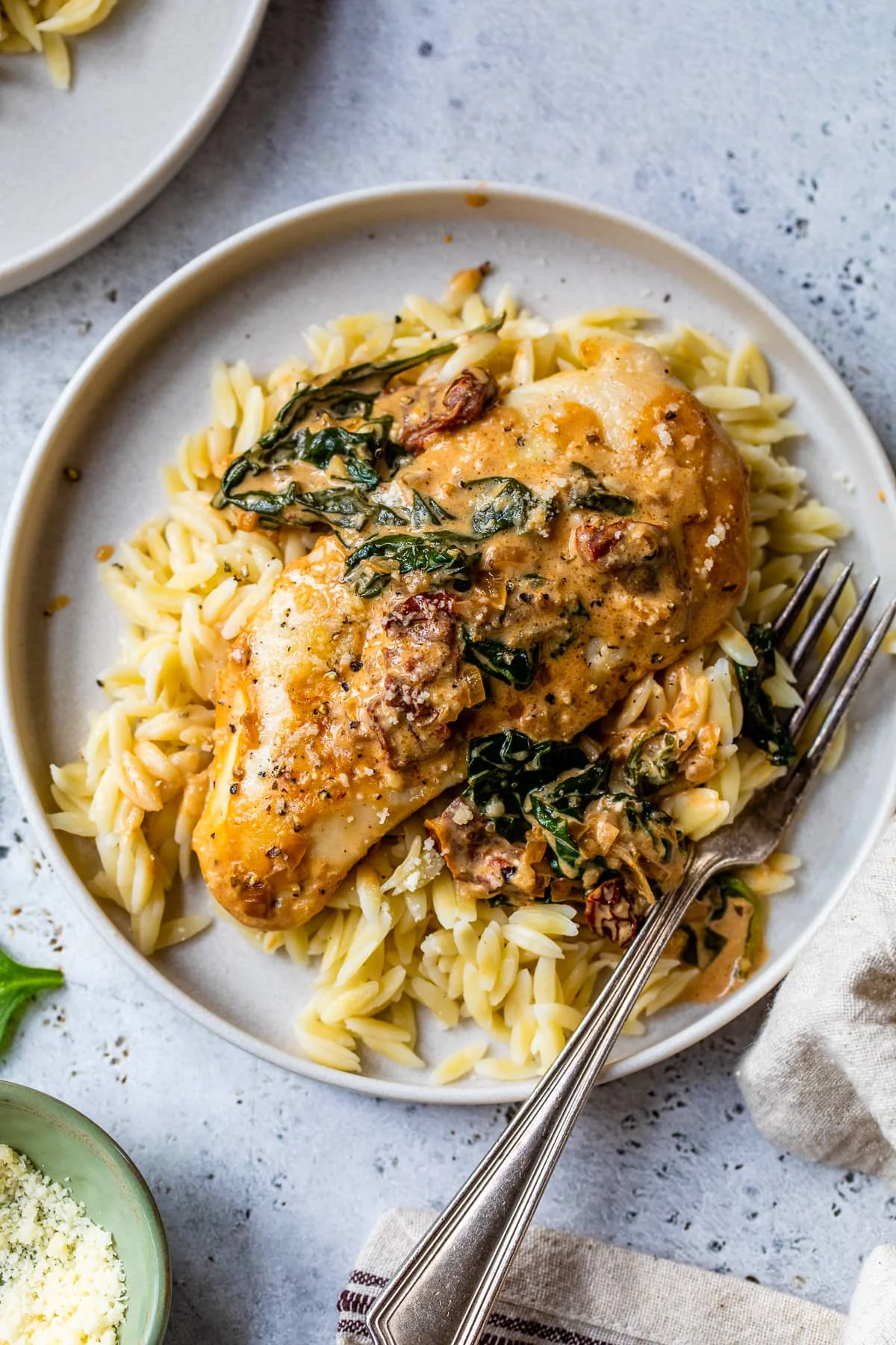Overhead view of Marry Me Chicken with spinach and sun-dried tomatoes served over orzo on a plate.