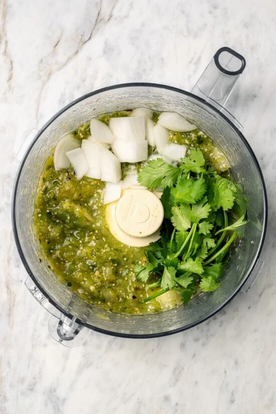 Overhead view of onion and cilantro added to salsa verde in food processor