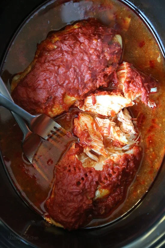 Overhead view of partially shredded harissa chicken inside the slow cooker.