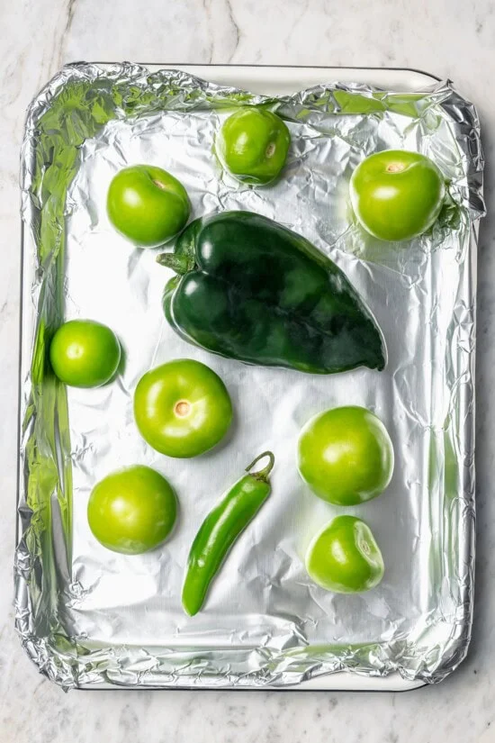 Overhead view of peppers and tomatillos on foil lined pan