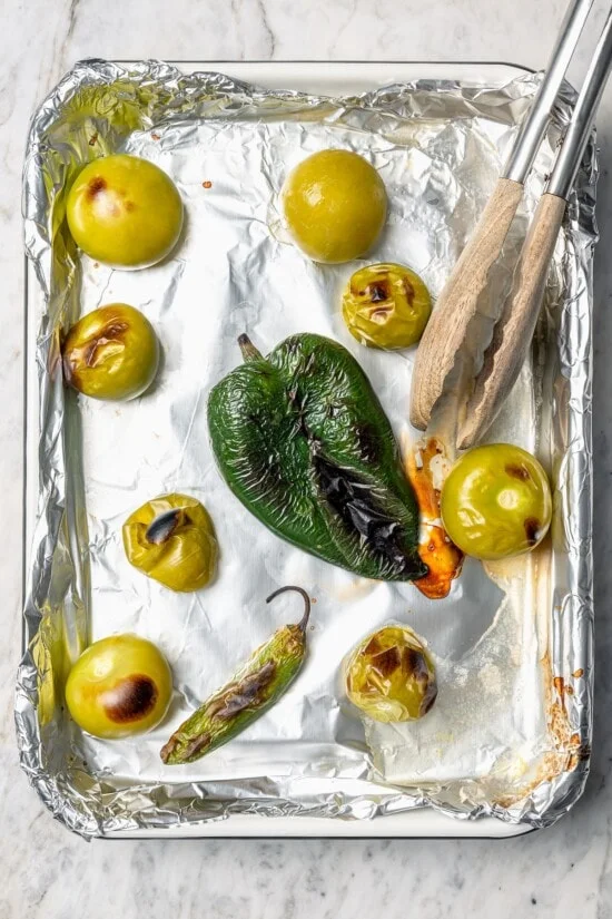 Overhead view of roasted peppers and tomatillos on foil lined pan