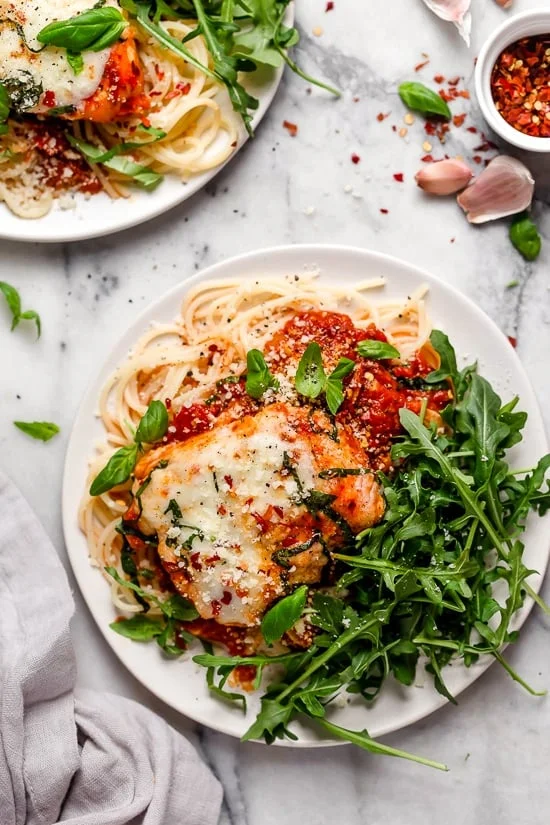 Overhead view of two plates of Instant Pot chicken parm with spaghetti noodles and greens