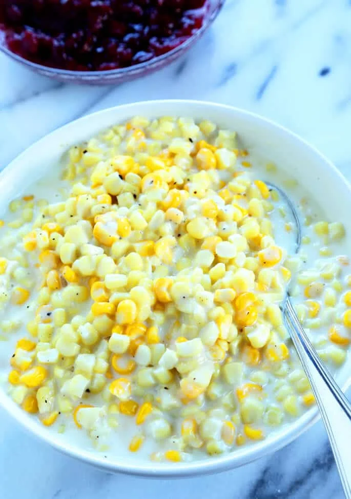 Overhead view off creamed corn in a white bowl with a metal spoon