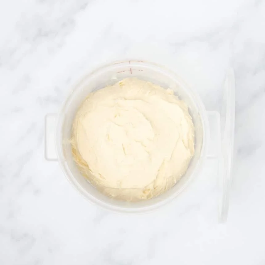 pale dough in clear round proofing bucket with cover on its side leaning against bucket