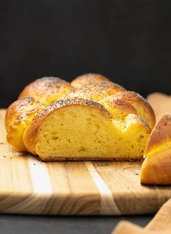 Partially sliced loaf of gluten free challah bread on cutting board with black background