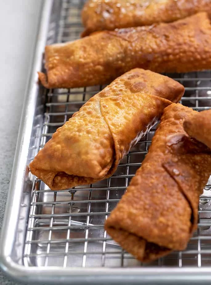 Parts of 5 fried egg rolls draining on wire rack atop metal baking tray