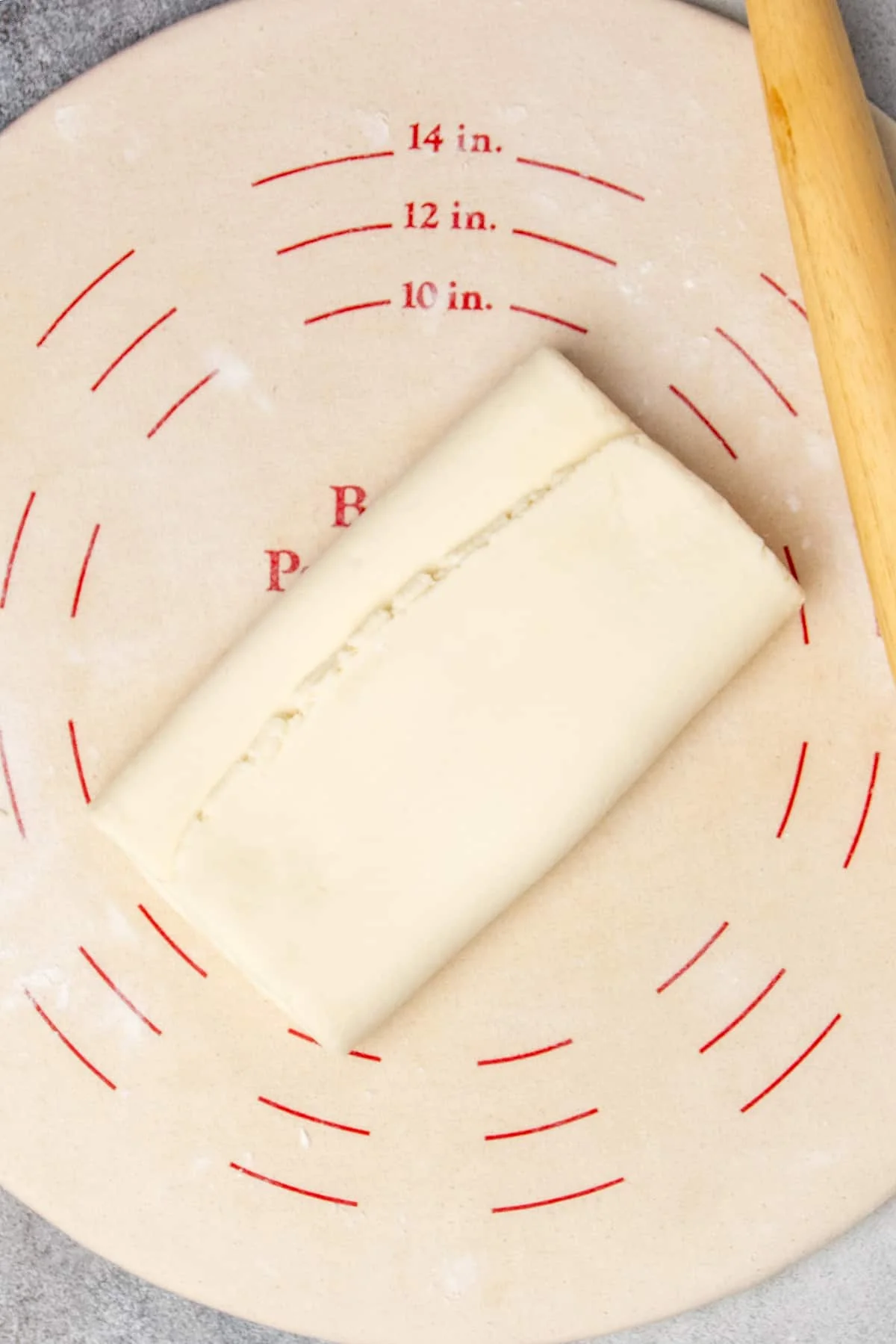 Pastry dough rolled out and folded in thirds like a business letter on light tan pastry board.