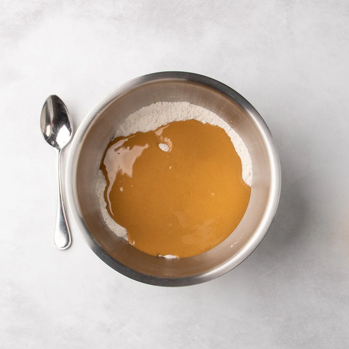 Peanut butter mixture poured into a metal mixing bowl on top of white dry ingredients.