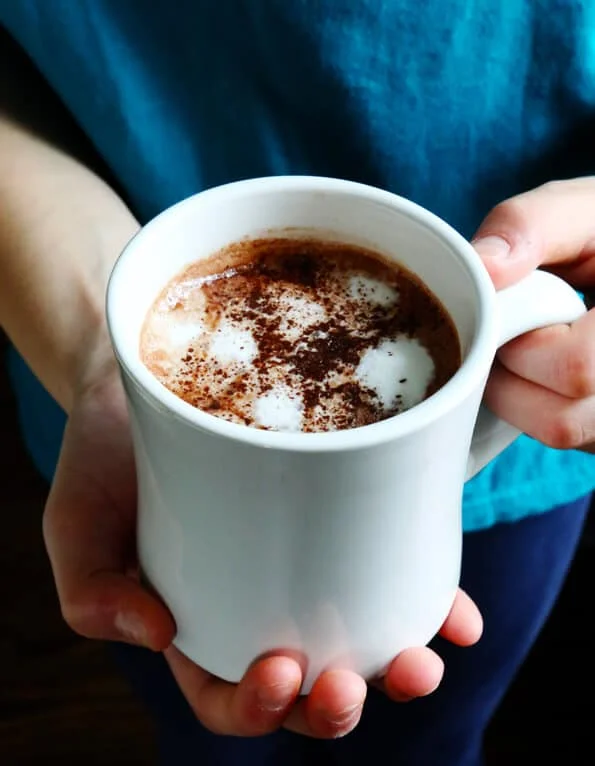 Person holding white mug with hot chocolate in mug 