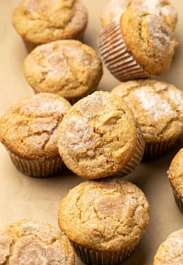 Pile of applesauce muffins in white liners on brown paper